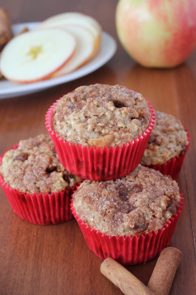 Four moist apple breakfast muffins in a pyramid with slices of apples and sticks of cinnamon in the for front and background.