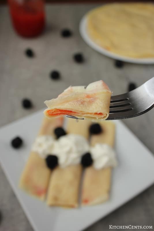 A bite of crepes filled with strawberry jam | KitchenCents.com