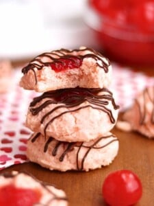 Three pink cookies with a cherry heart in the center drizzled with chocolate.