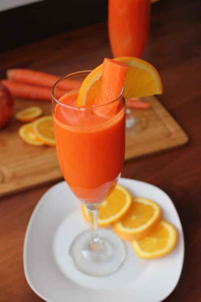A glass of Citrus Mocktail filled with a carrot stick and wedge of orange for garnish