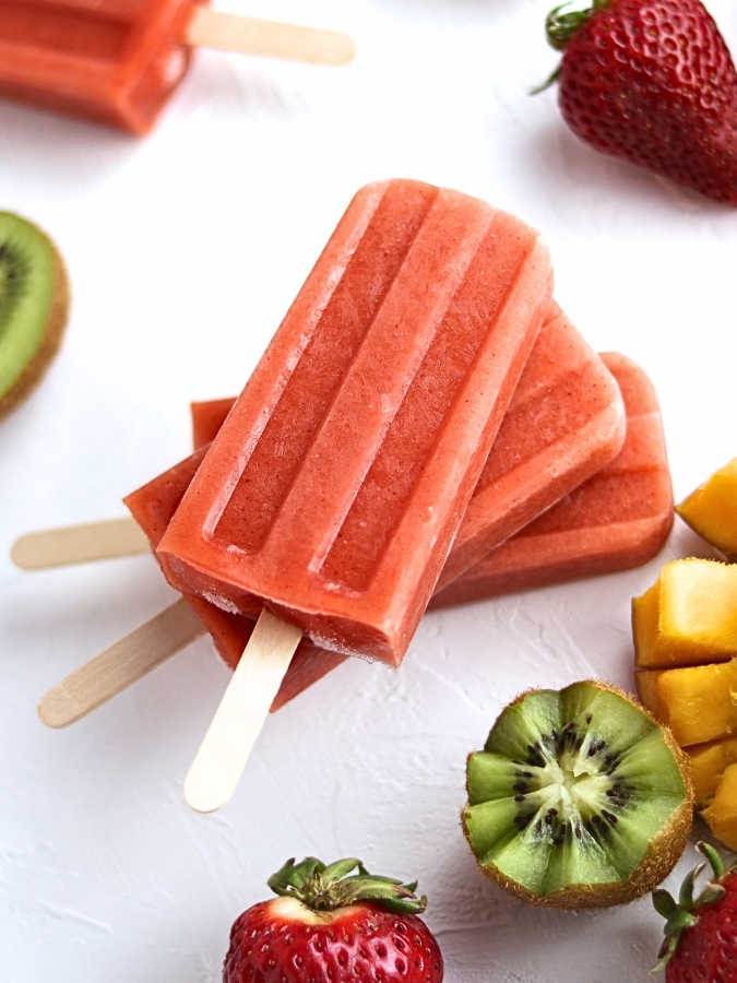 Smoothie popsicles stacked on top of each other with fresh fruit around them.