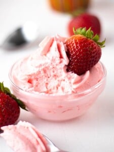 A small bowl filled with strawberry mousse with a whole fresh strawberry garnishing the side.