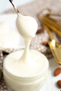 Homemade icing in a small glass bowl with a spoon dripping with the icing