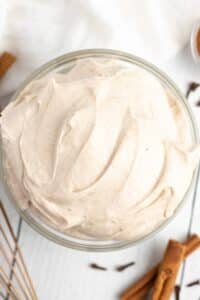 Pumpkin spice frosting in a glass bowl with cinnamon sticks and whole clove near it