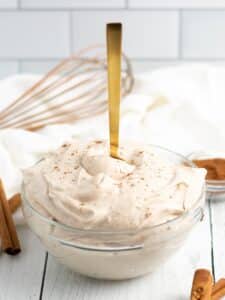 Spoon standing straight up in a bowl of pumpkin spice cream cheese frosting