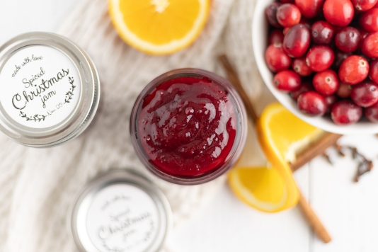 Full jar of cranberry jam with fresh cranberries and oranges around the jar.