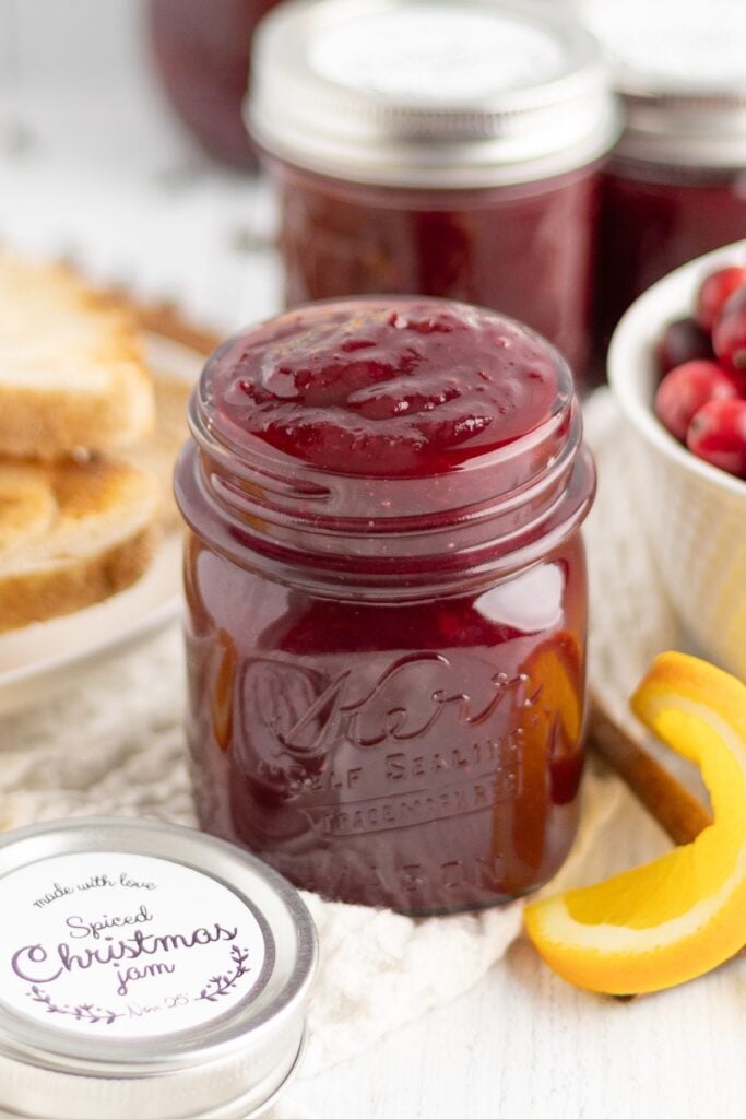 Full jar of cranberry Christmas jam with fresh cranberries and oranges around the jar.